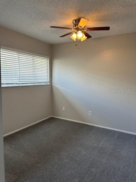 empty room featuring ceiling fan, baseboards, dark colored carpet, and a textured ceiling