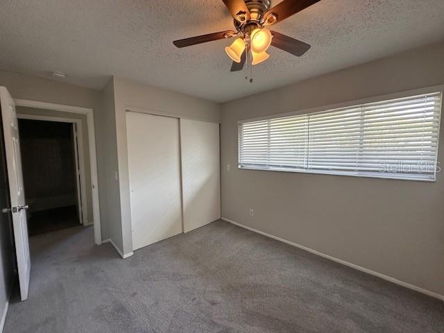 unfurnished bedroom featuring a textured ceiling, ceiling fan, carpet flooring, baseboards, and a closet