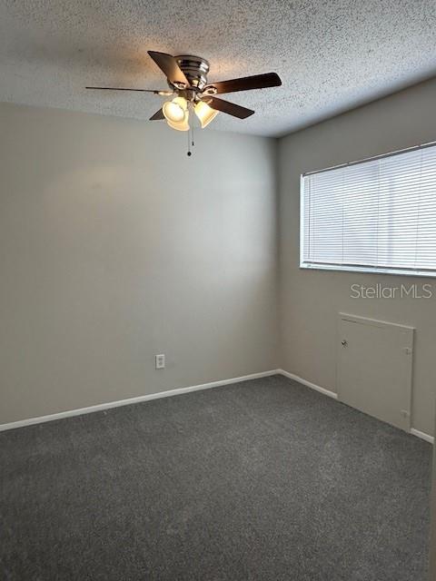 empty room with dark colored carpet, ceiling fan, a textured ceiling, and baseboards