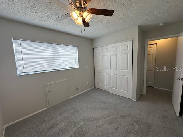 unfurnished bedroom featuring baseboards, a ceiling fan, a textured ceiling, carpet flooring, and a closet