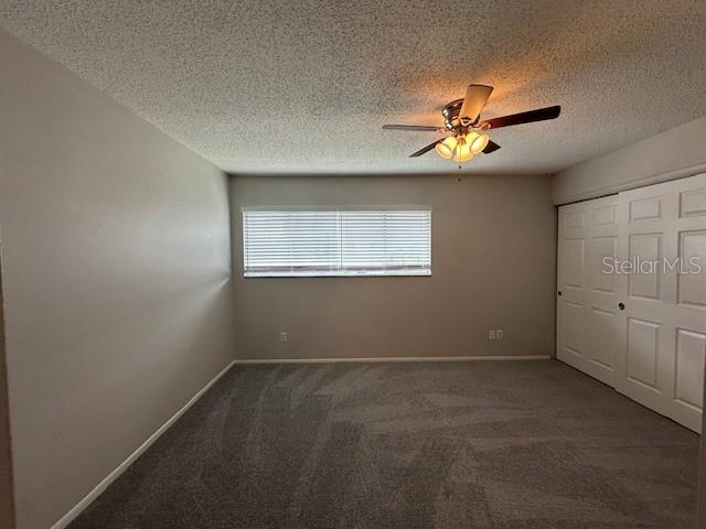 unfurnished bedroom with ceiling fan, dark colored carpet, a closet, and baseboards