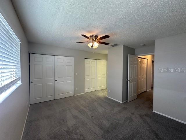 unfurnished bedroom featuring baseboards, visible vents, dark colored carpet, a textured ceiling, and multiple closets