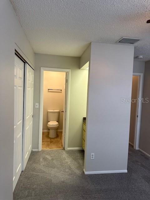 interior space featuring dark colored carpet, visible vents, a textured ceiling, and baseboards