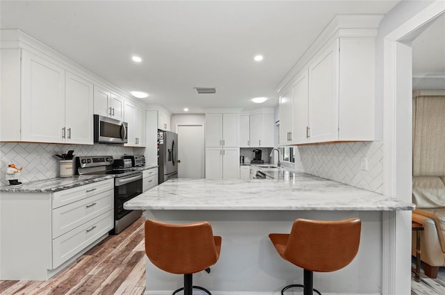 kitchen featuring visible vents, appliances with stainless steel finishes, a breakfast bar, a peninsula, and white cabinetry