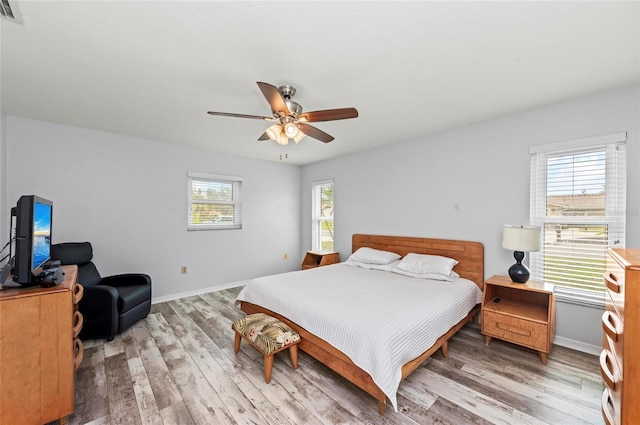 bedroom featuring a ceiling fan, visible vents, baseboards, and wood finished floors