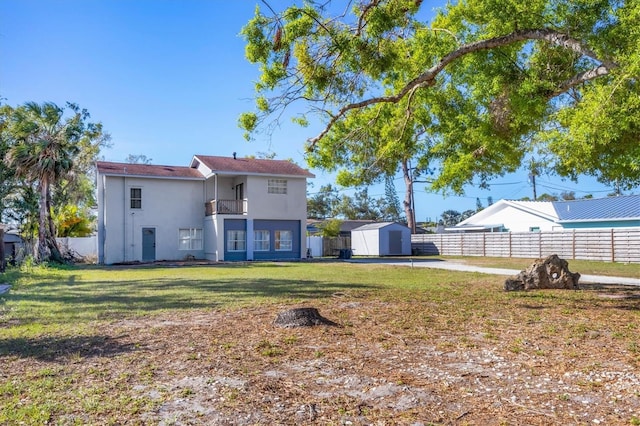 back of house with a storage shed, fence, a yard, an outdoor structure, and stucco siding