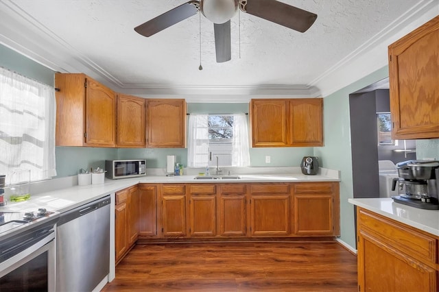 kitchen featuring stainless steel appliances, a sink, light countertops, ornamental molding, and dark wood-style floors