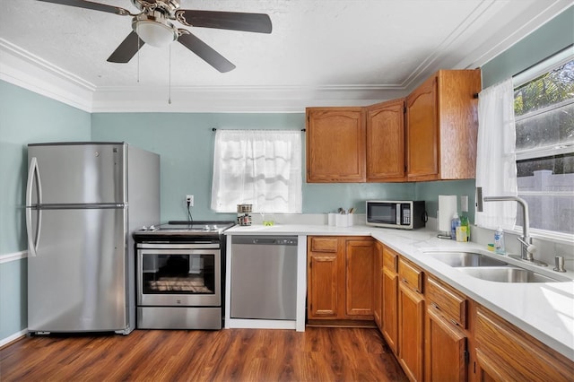 kitchen with dark wood finished floors, appliances with stainless steel finishes, ornamental molding, light countertops, and a sink