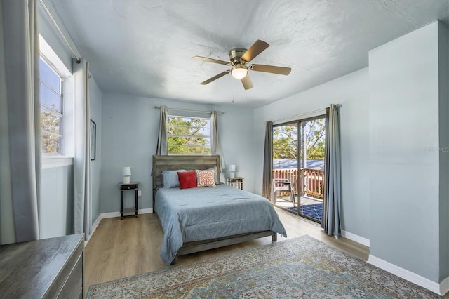 bedroom featuring access to exterior, multiple windows, baseboards, and wood finished floors