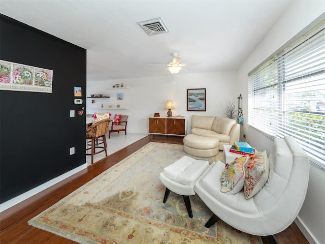 living room featuring a ceiling fan, baseboards, visible vents, and wood finished floors