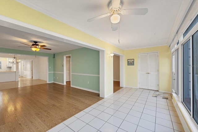 empty room featuring ceiling fan with notable chandelier, baseboards, crown molding, and light tile patterned flooring