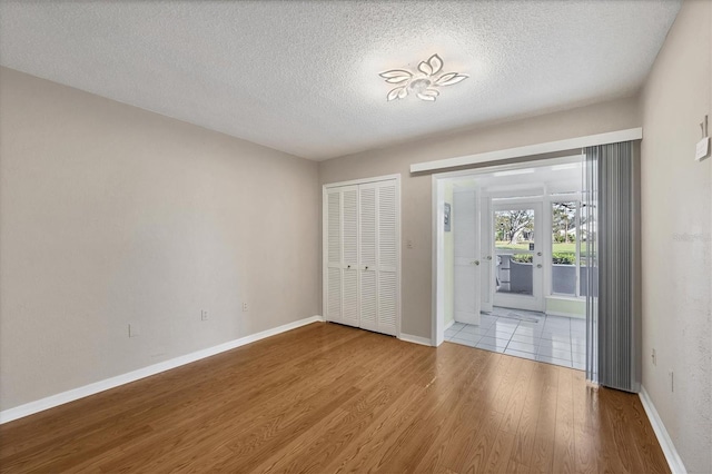 unfurnished bedroom featuring light wood-style flooring, a textured ceiling, baseboards, and a closet