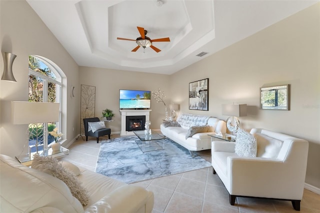 living area with a warm lit fireplace, visible vents, a raised ceiling, ceiling fan, and light tile patterned flooring