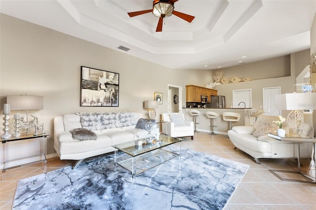 living area with a raised ceiling, visible vents, light tile patterned flooring, ceiling fan, and baseboards