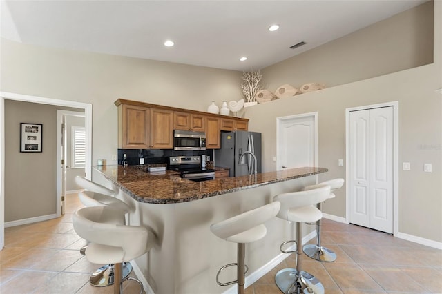 kitchen featuring light tile patterned floors, stainless steel appliances, a peninsula, a kitchen breakfast bar, and dark stone counters