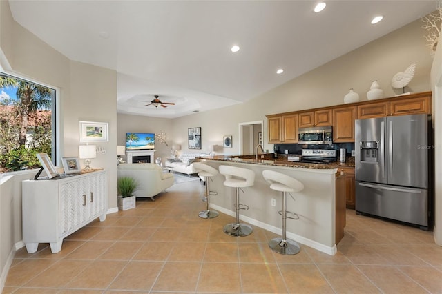 kitchen featuring a fireplace, open floor plan, appliances with stainless steel finishes, dark stone countertops, and a kitchen bar