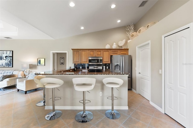 kitchen featuring light tile patterned floors, visible vents, appliances with stainless steel finishes, dark stone counters, and a kitchen bar