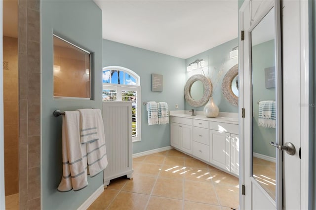 full bath featuring baseboards, double vanity, a sink, and tile patterned floors