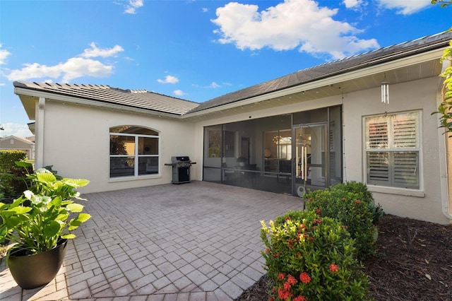 rear view of property featuring stucco siding, a sunroom, and a patio