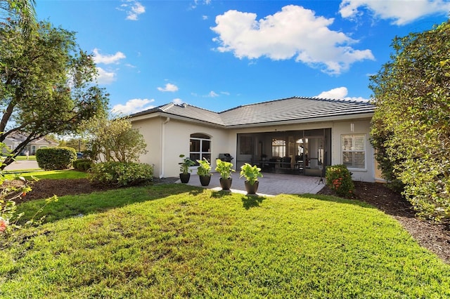 rear view of property with a patio, a lawn, a tiled roof, and stucco siding