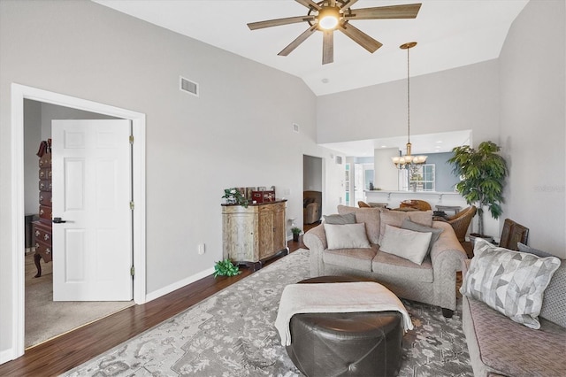 living area with high vaulted ceiling, ceiling fan with notable chandelier, wood finished floors, visible vents, and baseboards