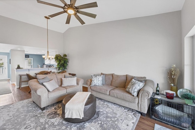 living area with lofted ceiling, baseboards, wood finished floors, and ceiling fan with notable chandelier