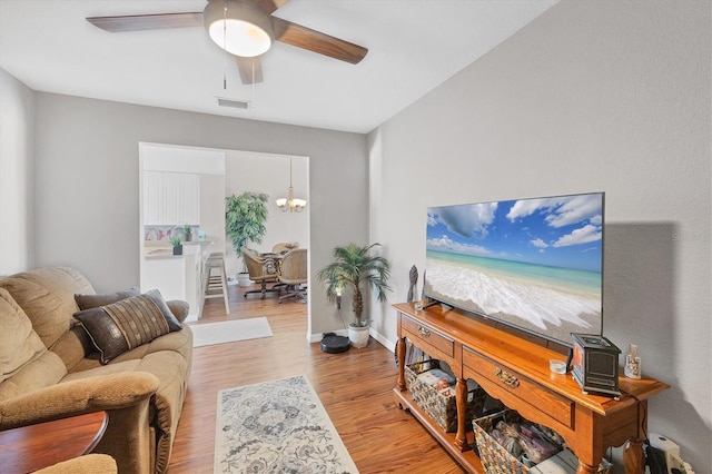 living room with ceiling fan with notable chandelier, wood finished floors, visible vents, and baseboards