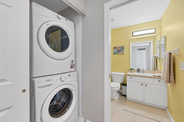 laundry room with visible vents, light tile patterned flooring, a sink, stacked washing maching and dryer, and baseboards