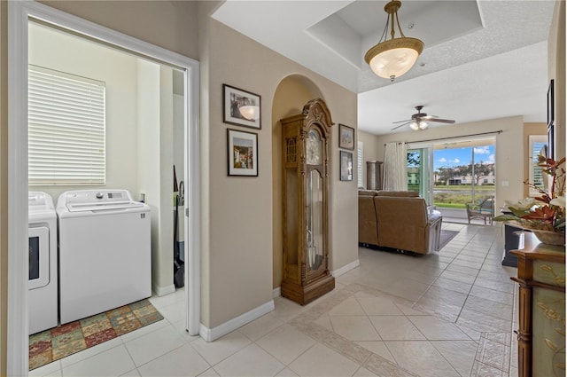 hall featuring arched walkways, light tile patterned floors, washing machine and dryer, and baseboards