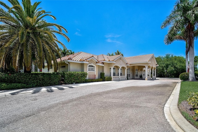 mediterranean / spanish home featuring covered porch, driveway, a tile roof, and stucco siding