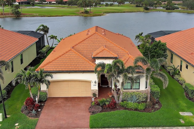 view of front of house with an attached garage, a water view, a tile roof, stone siding, and decorative driveway