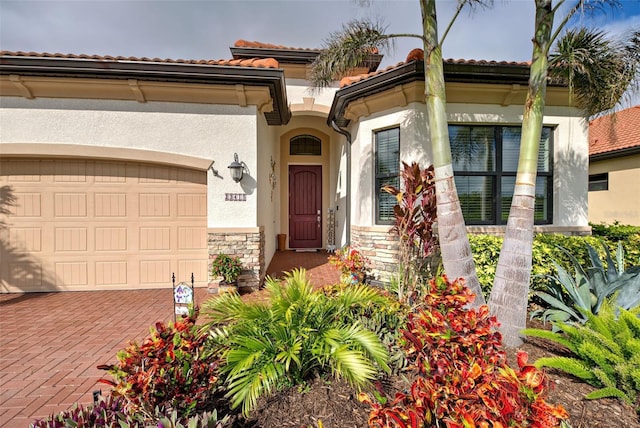 view of exterior entry featuring a garage, stone siding, a tiled roof, decorative driveway, and stucco siding