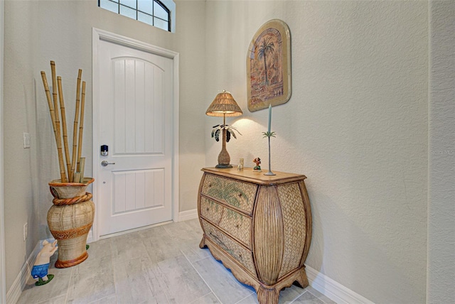 entrance foyer featuring a textured wall, light wood-style flooring, and baseboards