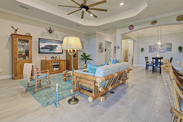 living room with arched walkways, ceiling fan, visible vents, ornamental molding, and a raised ceiling