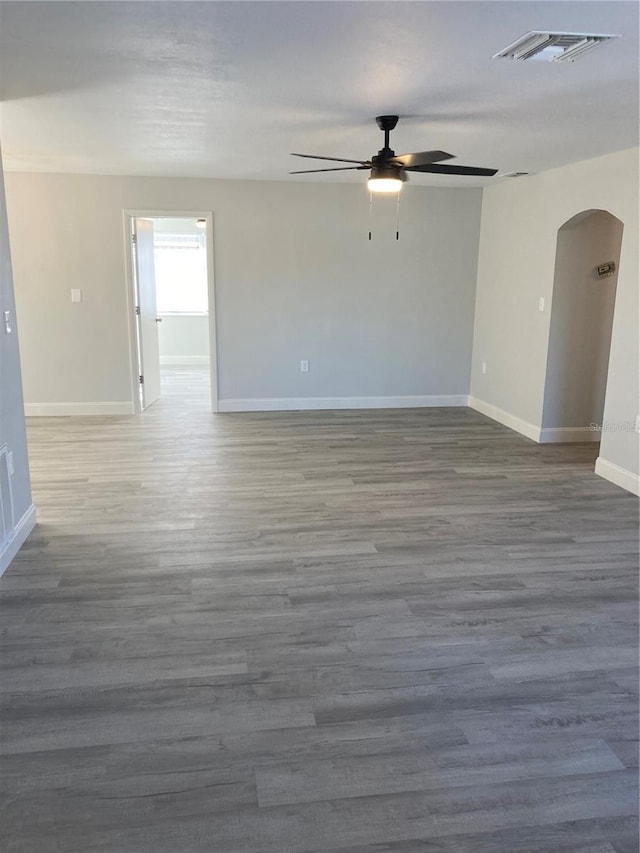 unfurnished room with arched walkways, visible vents, baseboards, and wood finished floors