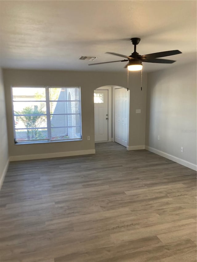 unfurnished room featuring arched walkways, visible vents, baseboards, and wood finished floors