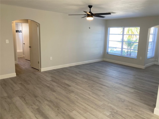 empty room with baseboards, arched walkways, and wood finished floors