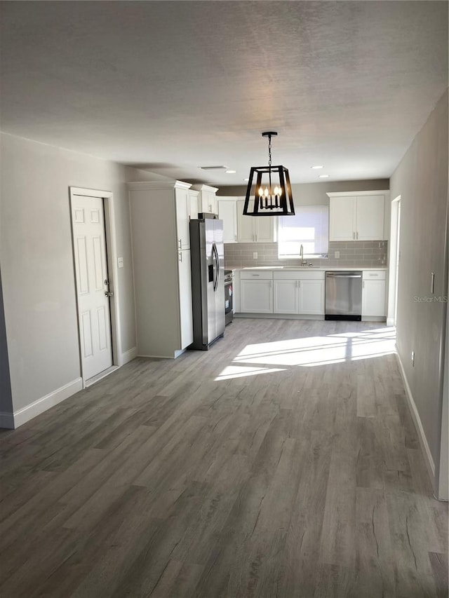 kitchen featuring hanging light fixtures, stainless steel appliances, light countertops, white cabinetry, and a sink