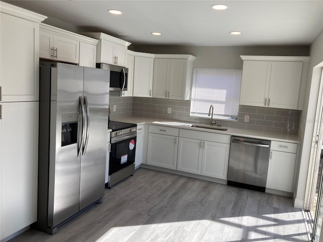 kitchen with light wood finished floors, white cabinets, appliances with stainless steel finishes, light countertops, and a sink