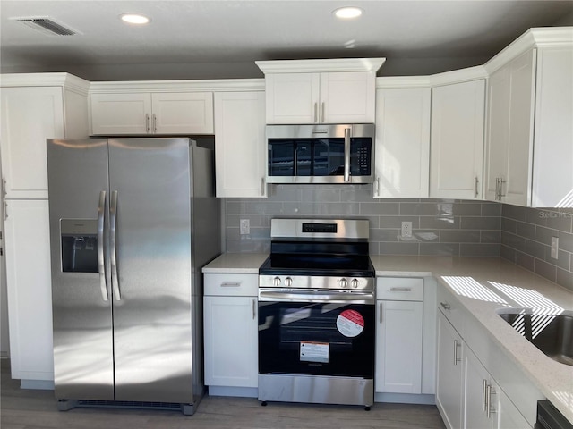 kitchen with visible vents, decorative backsplash, appliances with stainless steel finishes, light countertops, and white cabinetry