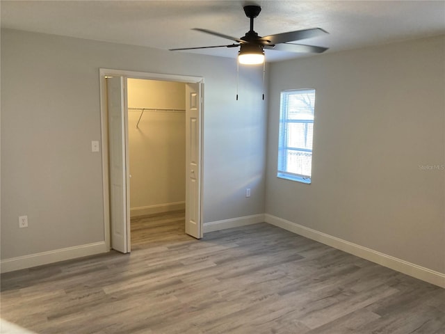 unfurnished bedroom with wood finished floors, a ceiling fan, baseboards, a spacious closet, and a closet