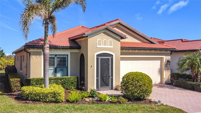 mediterranean / spanish-style home with a garage, a tile roof, decorative driveway, and stucco siding