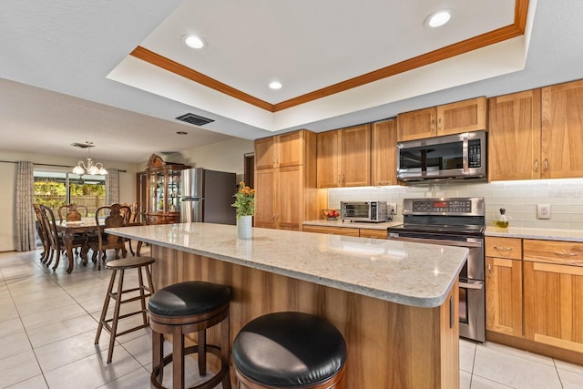 kitchen featuring stainless steel appliances, a tray ceiling, visible vents, and decorative backsplash