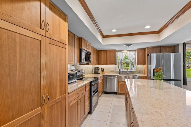 kitchen featuring stainless steel appliances, a sink, decorative backsplash, a raised ceiling, and crown molding