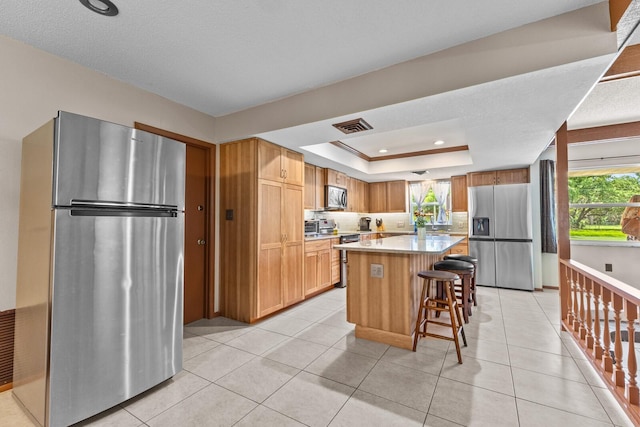 kitchen with a raised ceiling, appliances with stainless steel finishes, a breakfast bar, light countertops, and light tile patterned flooring