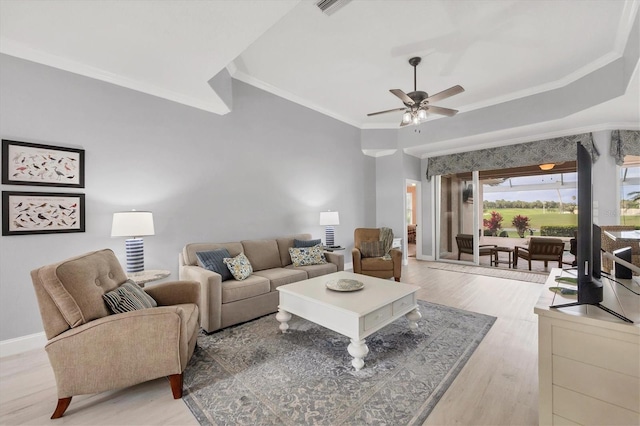 living area with a tray ceiling, ornamental molding, light wood-style floors, a ceiling fan, and baseboards