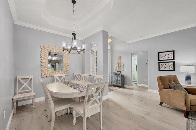 dining space with baseboards, a raised ceiling, light wood-style flooring, and crown molding