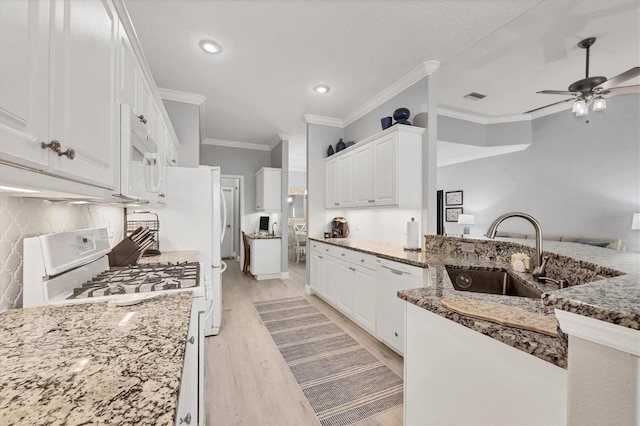 kitchen with light wood finished floors, white cabinets, a sink, dark stone counters, and white appliances