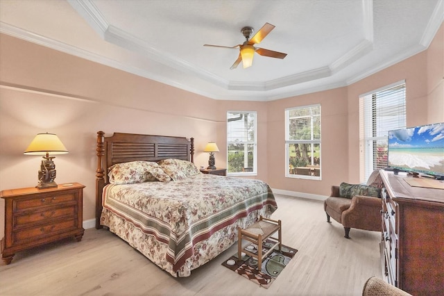 bedroom with baseboards, light wood-type flooring, a raised ceiling, and crown molding