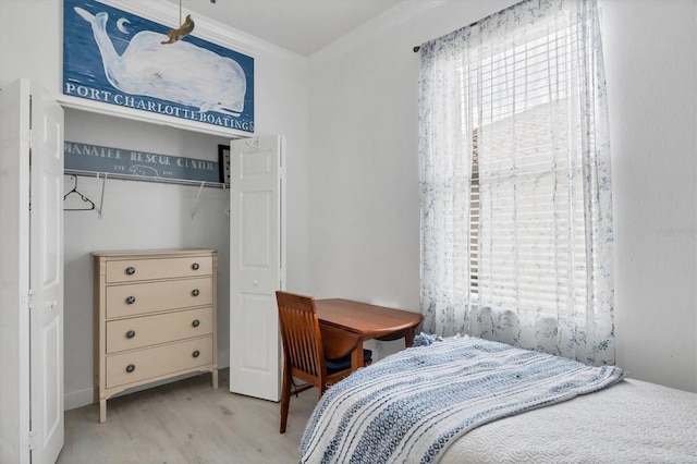 bedroom with light wood finished floors, a closet, and crown molding